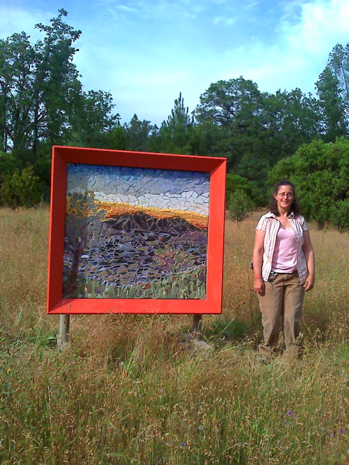 Picture of 4 foot by 4foot "lake county Landscape installed along the trail at Middletown County Park. Artist Alicia Lee Farnsworth Stands beside the sculpture.